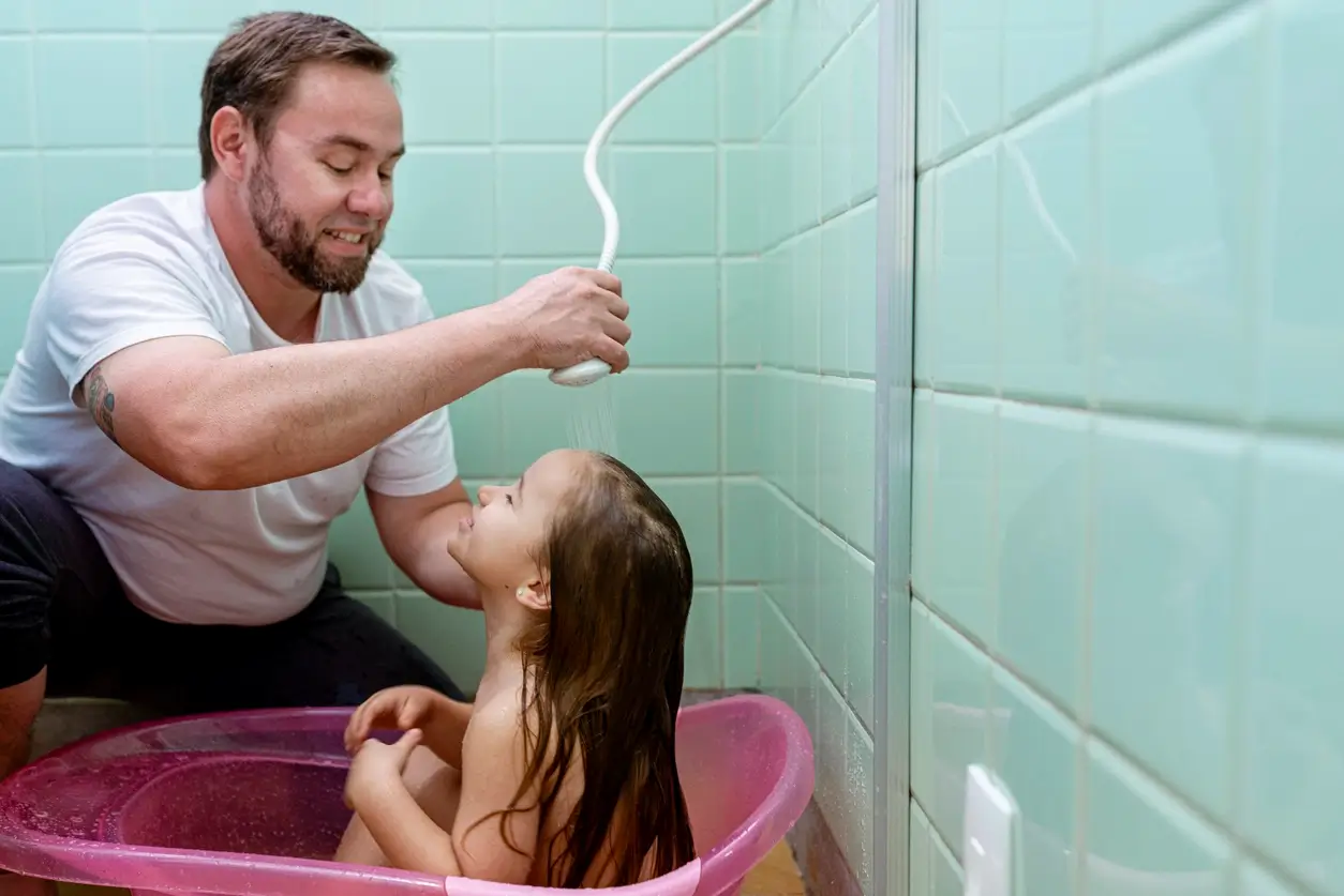 Pai dando banho na sua filha com o chuveiro a gás, economizando mais energia do que o chuveiro elétrico